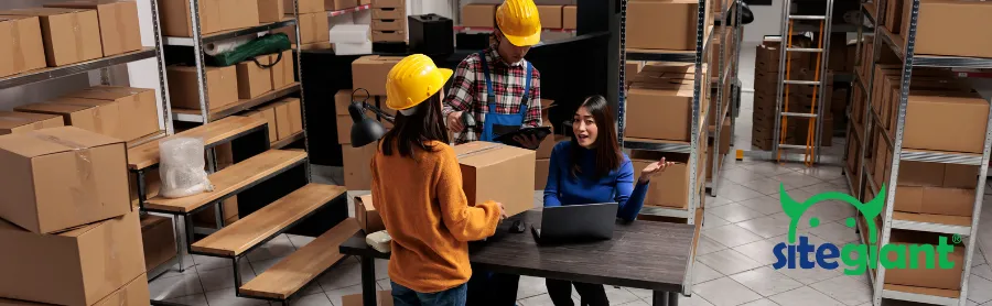 three staff are discussing in a warehouse with boxes